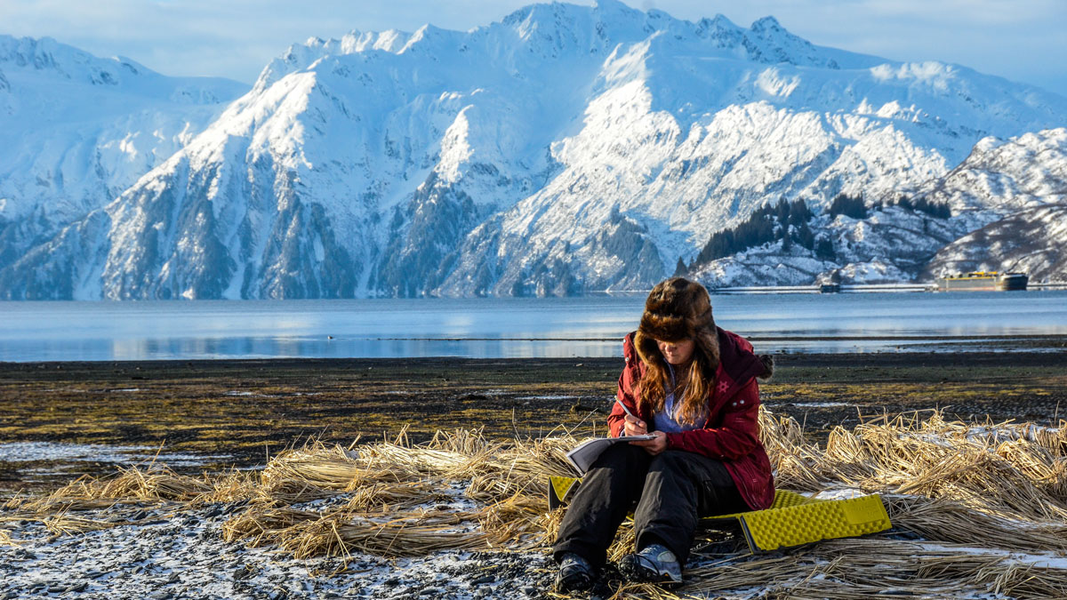 Prince William Sound College student sits on a beach and writes in Valdez, Alaska