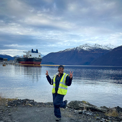 A girl in safety gear on a beach with tanker in background.