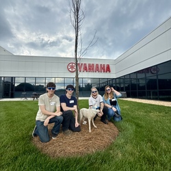 Four people facing camera at a Yamaha facilty. 