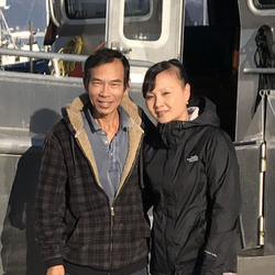 Man and woman smiling at camera. They are outside by skiff.