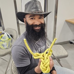 Man sitting in chair holding up a knotted piece of rope.