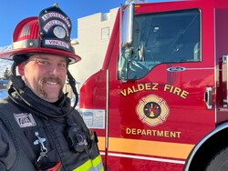 Fireman smiling and standing beside firetruck.