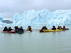 Several people in kayaks by glacier.
