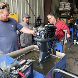 Three men working on an outboard engine. 