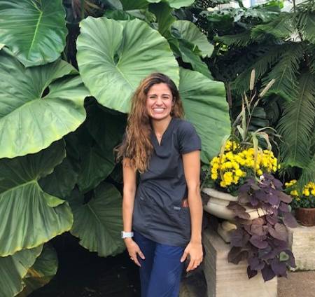 student in scrubs standing in front of plants