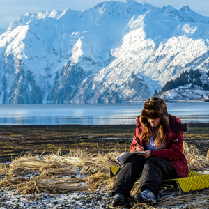 Student writing next to the ocean in Valdez, Alaska