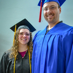 Larissa Williams, PWSC Graduate, stands in a graduation cap and gown with her husband.