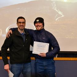 Instructor and graduate together smiling and graduate holding his certificate. 
