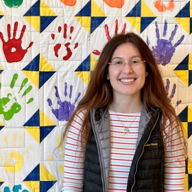 Shelby standing in front of quilt with child handprints